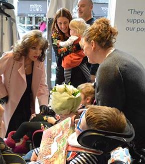 Joan Collins with customers and children at Shooting Star Chase shop in Fulham